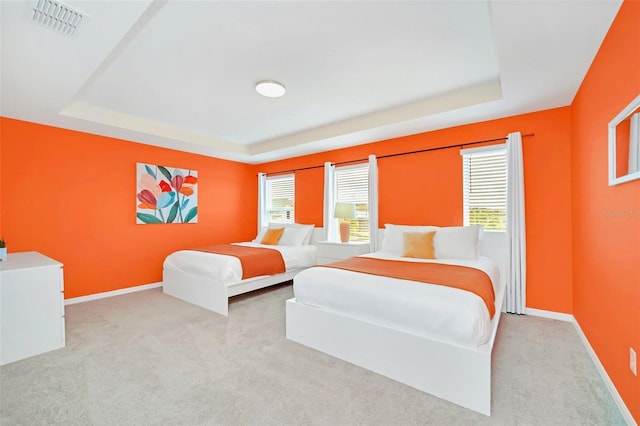 bedroom with light colored carpet and a tray ceiling