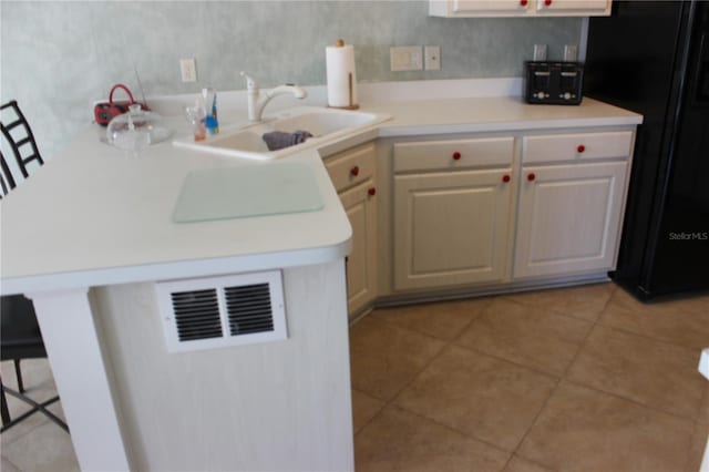 kitchen featuring cream cabinetry, black fridge, sink, a breakfast bar area, and light tile patterned floors