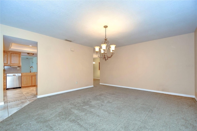 carpeted spare room with a tray ceiling and a chandelier