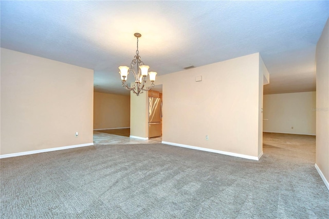 carpeted spare room with an inviting chandelier