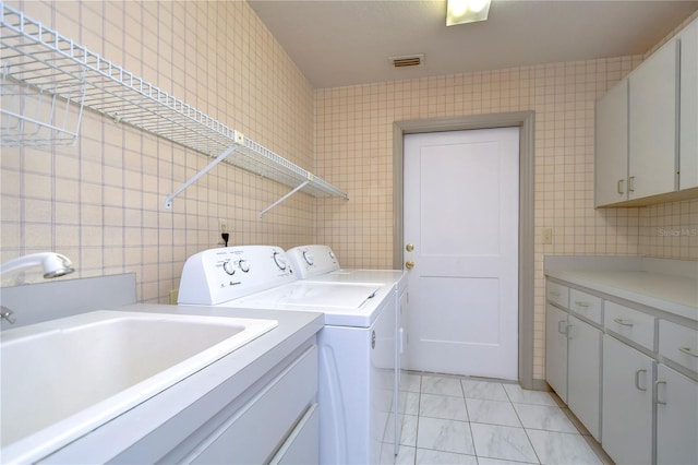 clothes washing area with light tile patterned floors, tile walls, washer and clothes dryer, and cabinets