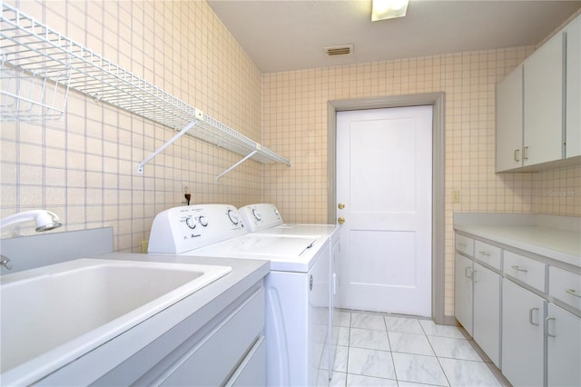 laundry area with washing machine and clothes dryer, tile walls, cabinets, and light tile patterned floors