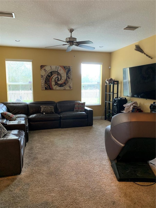 carpeted living area with a wealth of natural light, visible vents, a textured ceiling, and ceiling fan