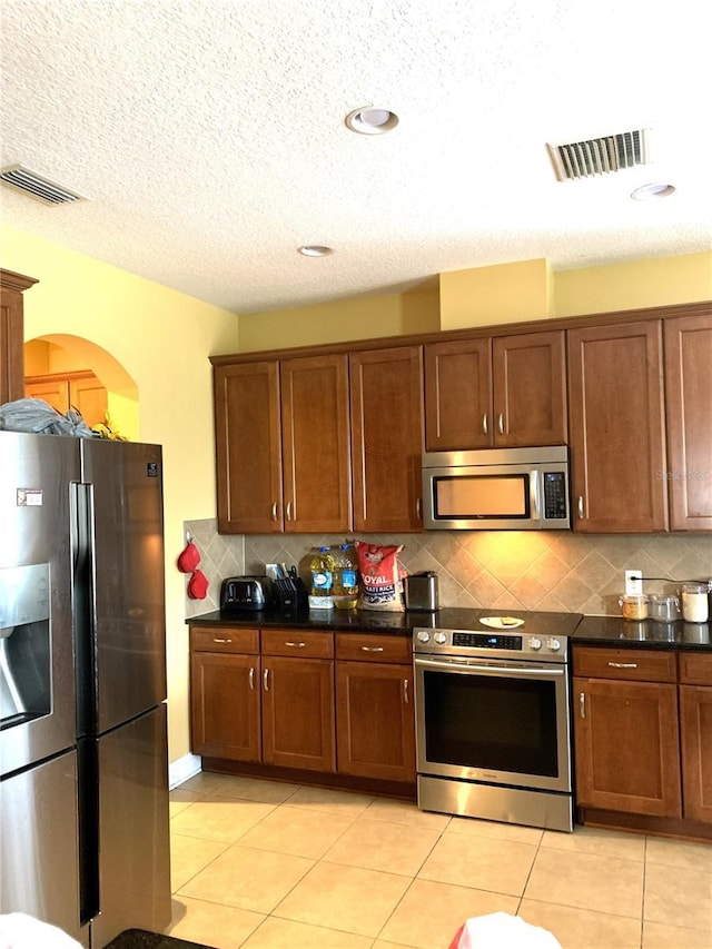 32502 Summerglade Dr, Wesley Chapel, FL 33545 - kitchen featuring stainless steel appliances, backsplash, dark countertops, light tile patterned flooring, and arched walkways