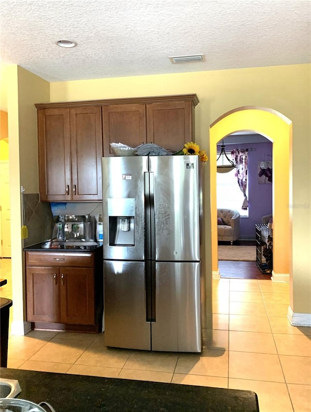 kitchen featuring a textured ceiling, stainless steel refrigerator with ice dispenser, decorative backsplash, and light tile patterned flooring