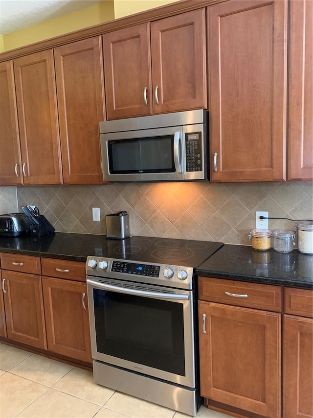 kitchen with dark stone counters, backsplash, light tile patterned flooring, and stainless steel appliances