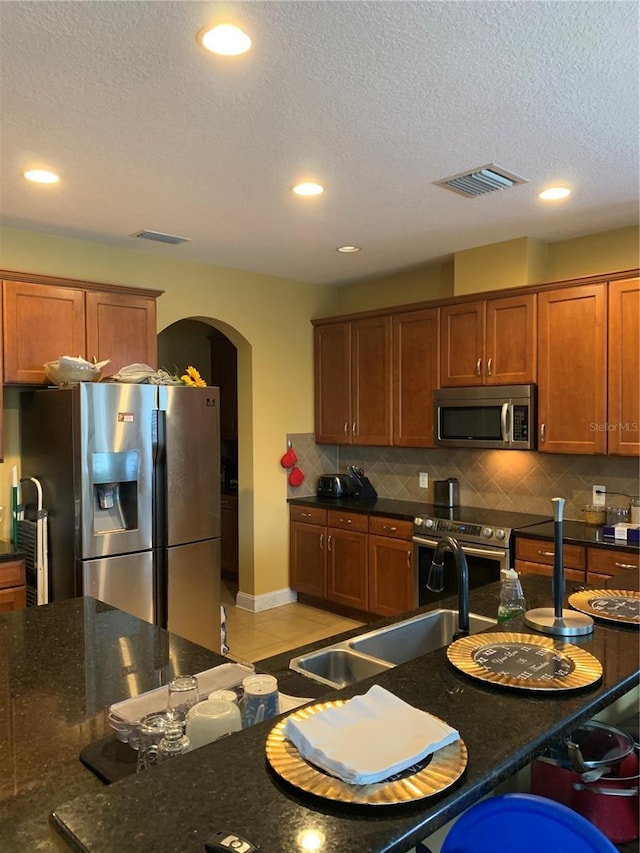 32502 Summerglade Dr, Wesley Chapel, FL 33545 - kitchen with stainless steel appliances, arched walkways, backsplash, brown cabinetry, and recessed lighting