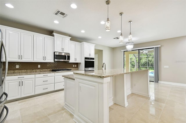 kitchen with light stone countertops, white cabinetry, pendant lighting, a kitchen island with sink, and appliances with stainless steel finishes