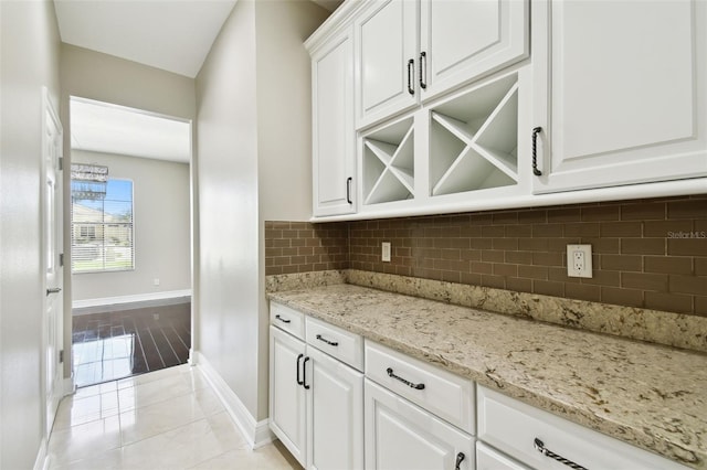 bar featuring white cabinets, light stone countertops, light wood-type flooring, and backsplash