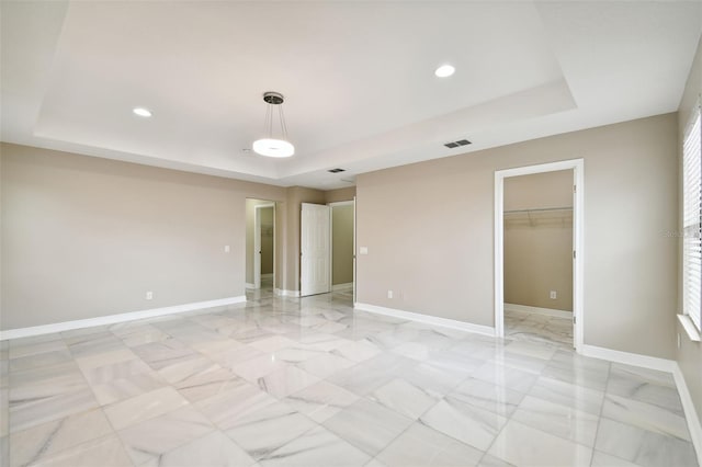 unfurnished bedroom with a walk in closet, a raised ceiling, and a closet