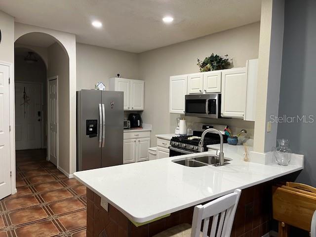 kitchen featuring sink, appliances with stainless steel finishes, white cabinets, a kitchen bar, and kitchen peninsula