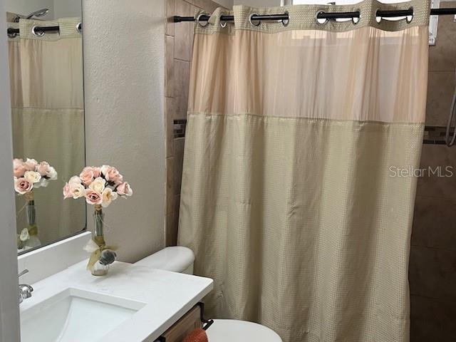 bathroom featuring toilet, vanity, a shower with shower curtain, and a textured wall