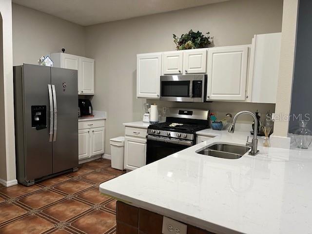 kitchen with dark tile patterned flooring, a sink, white cabinets, light countertops, and appliances with stainless steel finishes