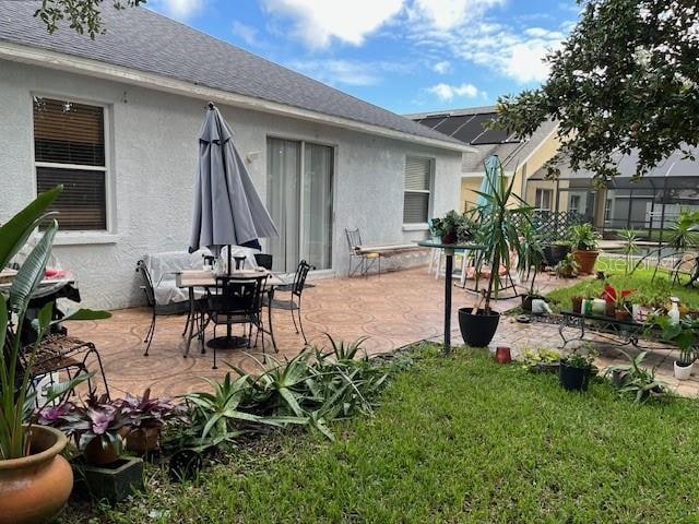 exterior space with a patio area, roof with shingles, a lawn, and stucco siding