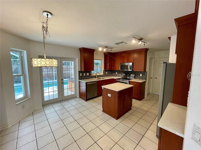 kitchen with backsplash, a kitchen island, hanging light fixtures, appliances with stainless steel finishes, and track lighting