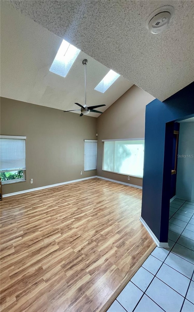 spare room featuring light wood-type flooring, a textured ceiling, a healthy amount of sunlight, and lofted ceiling with skylight