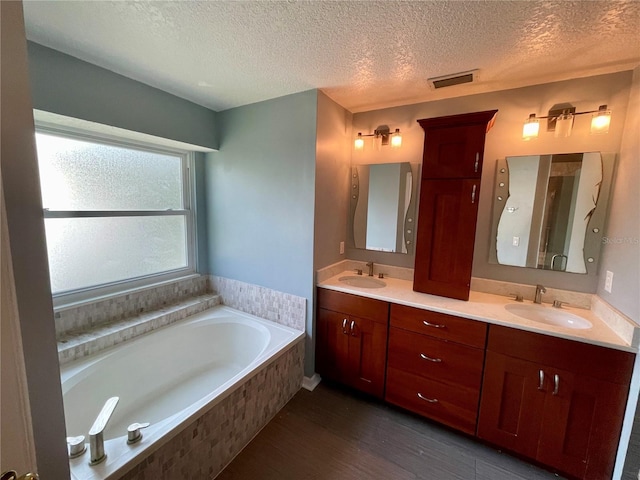 bathroom with a textured ceiling, hardwood / wood-style flooring, tiled tub, and vanity