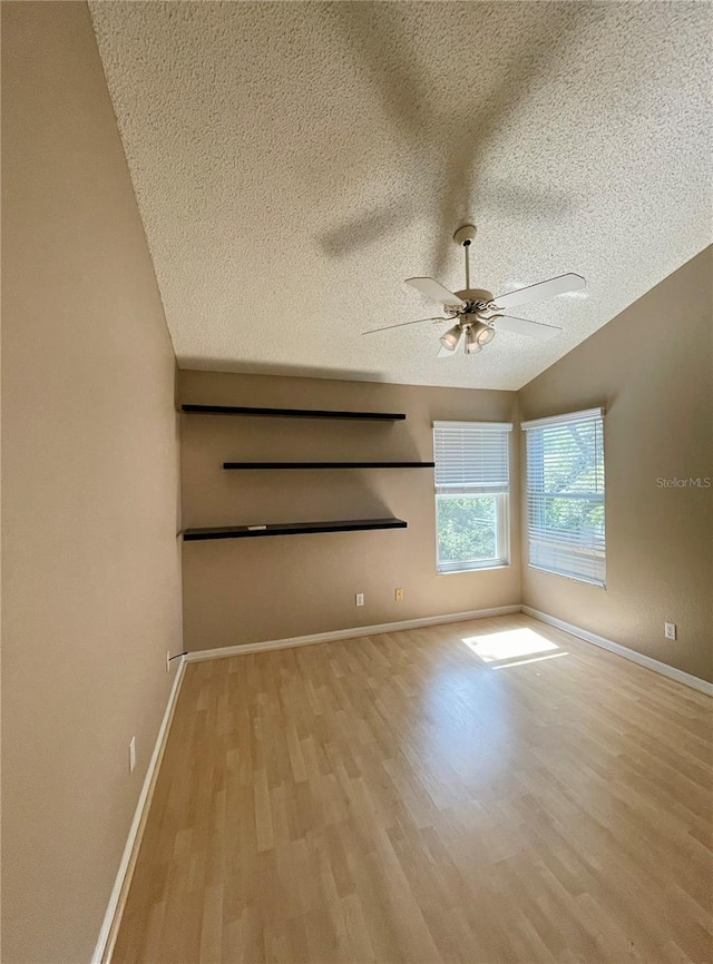 empty room with ceiling fan, a textured ceiling, light hardwood / wood-style flooring, and lofted ceiling