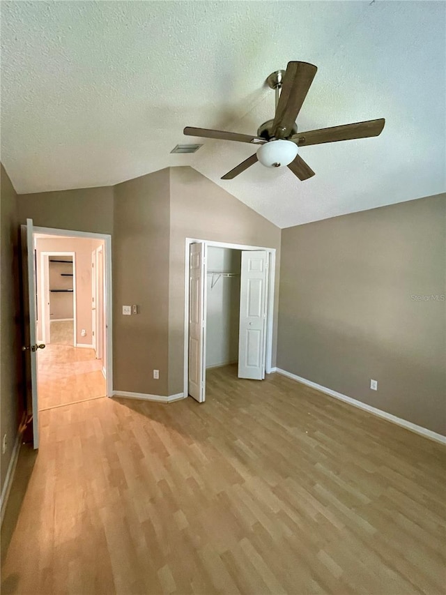 unfurnished bedroom with ceiling fan, a closet, a textured ceiling, vaulted ceiling, and light hardwood / wood-style flooring