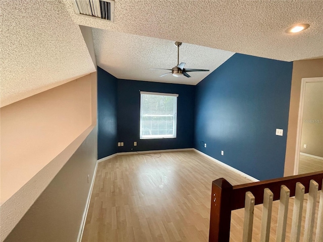 unfurnished room featuring ceiling fan, a textured ceiling, light hardwood / wood-style flooring, and vaulted ceiling