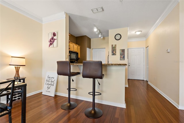 kitchen featuring kitchen peninsula, light stone counters, ornamental molding, a breakfast bar, and dark hardwood / wood-style floors