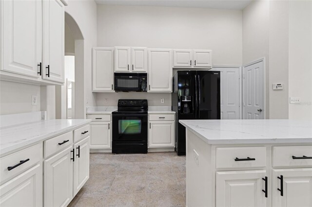 kitchen with white cabinetry, light tile patterned floors, black appliances, and light stone countertops