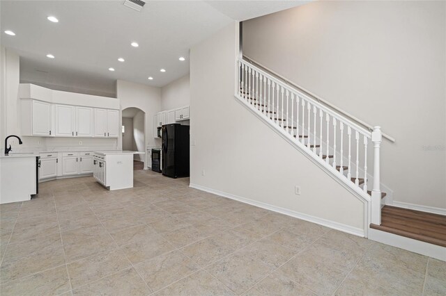 kitchen featuring light hardwood / wood-style flooring, white cabinetry, sink, black refrigerator, and a center island