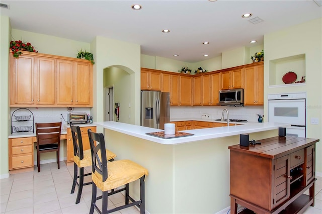 kitchen featuring light tile patterned floors, stainless steel appliances, decorative backsplash, a breakfast bar area, and kitchen peninsula