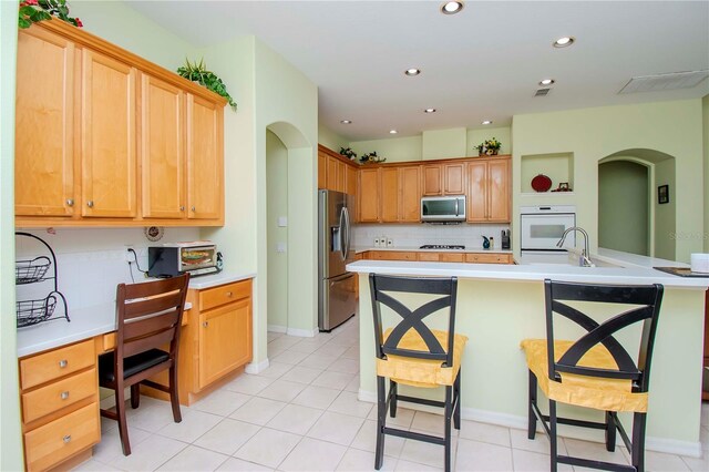 kitchen featuring tasteful backsplash, appliances with stainless steel finishes, light tile patterned floors, and a kitchen bar