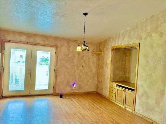 unfurnished dining area featuring light wood-type flooring, a notable chandelier, french doors, and a textured ceiling