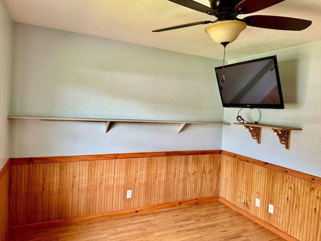 empty room with ceiling fan, light hardwood / wood-style flooring, and wooden walls