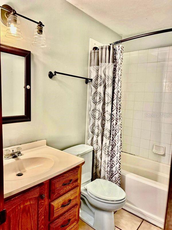 full bathroom with shower / bath combo with shower curtain, tile patterned floors, a textured ceiling, vanity, and toilet