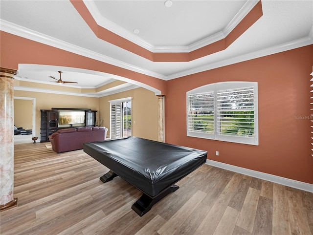 game room featuring crown molding, a tray ceiling, decorative columns, and light hardwood / wood-style flooring