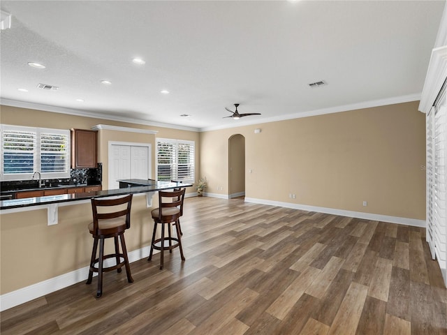 kitchen with ceiling fan, ornamental molding, a breakfast bar area, and dark hardwood / wood-style floors