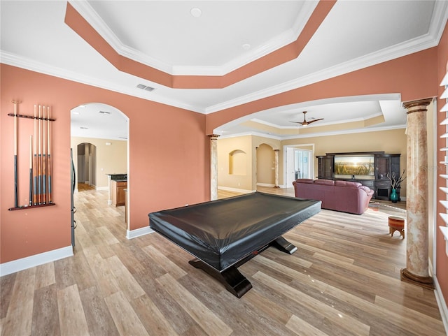 playroom with ceiling fan, a raised ceiling, light wood-type flooring, ornate columns, and crown molding