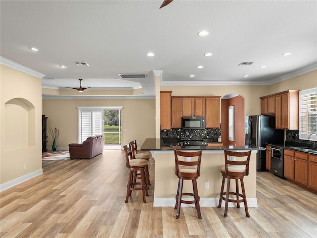 kitchen featuring a kitchen breakfast bar, light hardwood / wood-style flooring, ornamental molding, black appliances, and sink