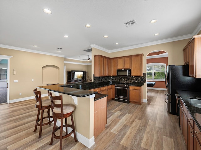 kitchen with kitchen peninsula, a breakfast bar area, appliances with stainless steel finishes, light hardwood / wood-style flooring, and ornamental molding