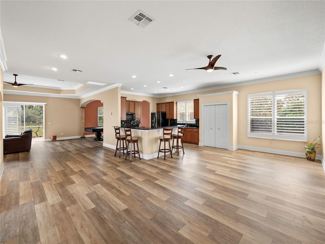 kitchen with black appliances, crown molding, light hardwood / wood-style floors, and a breakfast bar