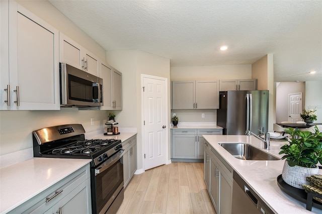 kitchen featuring appliances with stainless steel finishes, light hardwood / wood-style floors, sink, and a textured ceiling