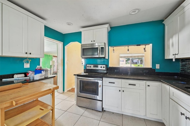 kitchen with white cabinetry, appliances with stainless steel finishes, dark stone counters, and light tile patterned floors