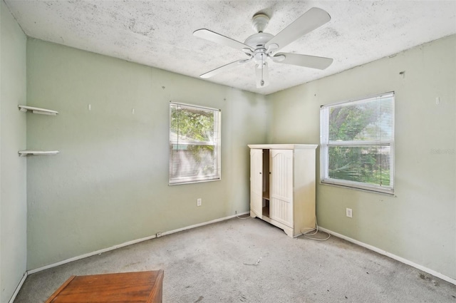 unfurnished bedroom featuring multiple windows, light carpet, a textured ceiling, and ceiling fan