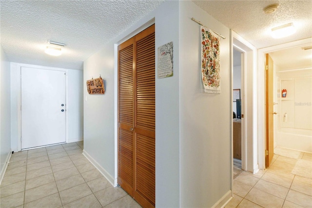 corridor with a textured ceiling and light tile patterned flooring