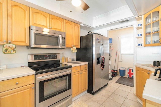 kitchen with light tile patterned flooring, ornamental molding, a tray ceiling, ceiling fan, and stainless steel appliances