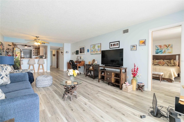 living room featuring ceiling fan, a textured ceiling, and light hardwood / wood-style flooring