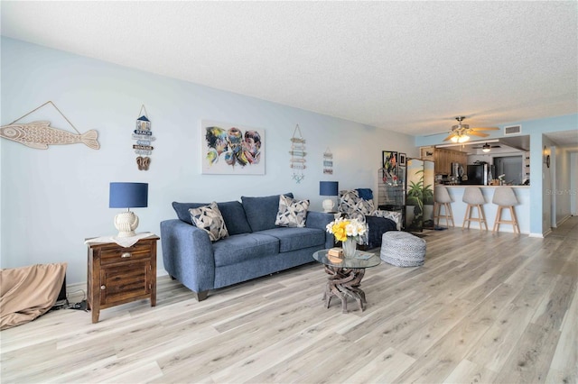 living room featuring ceiling fan, a textured ceiling, and light wood-type flooring