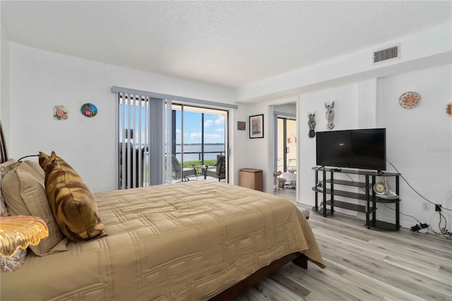 bedroom with access to outside, a textured ceiling, and light hardwood / wood-style flooring