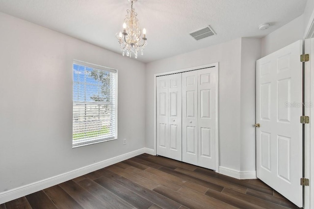 unfurnished bedroom with dark hardwood / wood-style flooring, a closet, and a chandelier