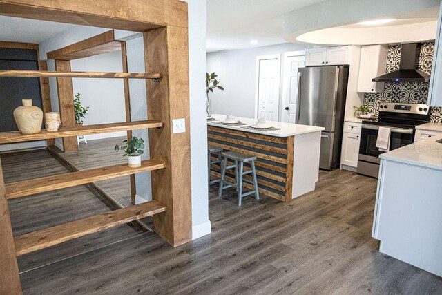 kitchen featuring white cabinets, dark hardwood / wood-style flooring, appliances with stainless steel finishes, and wall chimney range hood