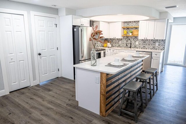 kitchen with tasteful backsplash, stainless steel appliances, white cabinets, dark hardwood / wood-style floors, and a breakfast bar