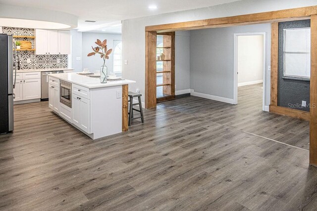 kitchen with stainless steel appliances, a center island with sink, white cabinetry, a kitchen breakfast bar, and dark wood-type flooring